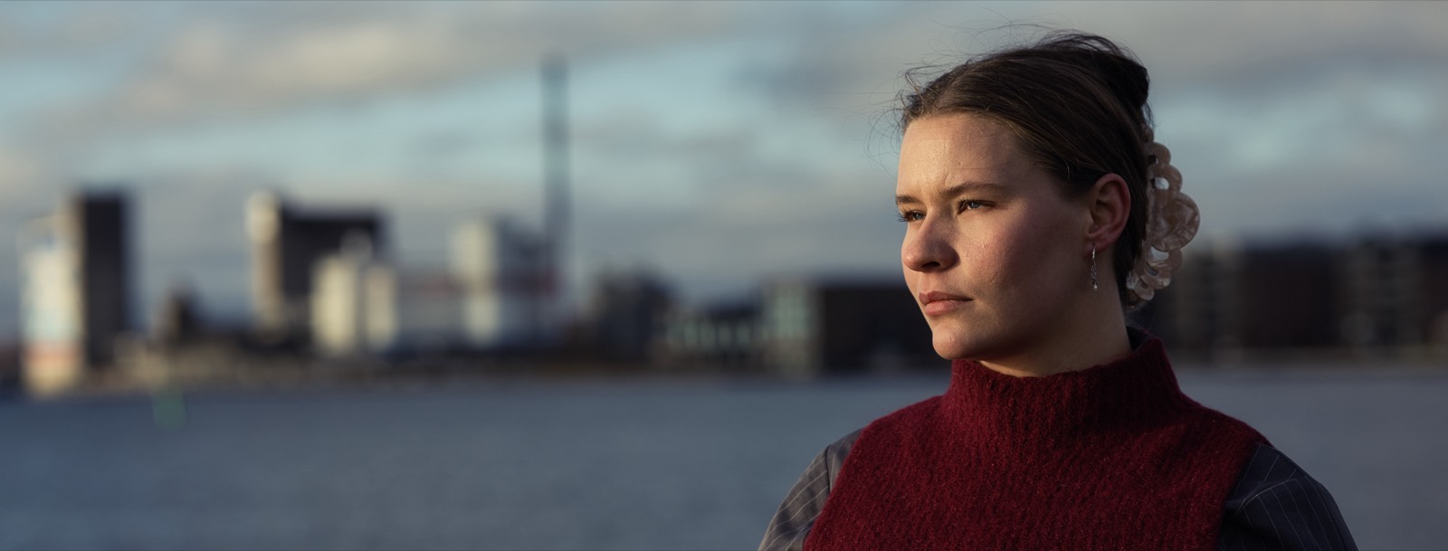 Maria-Louise Lundqvist i rød strikvest står ved havnen og kigger ud over vandet. Bag hende ses byen i det fjerne.